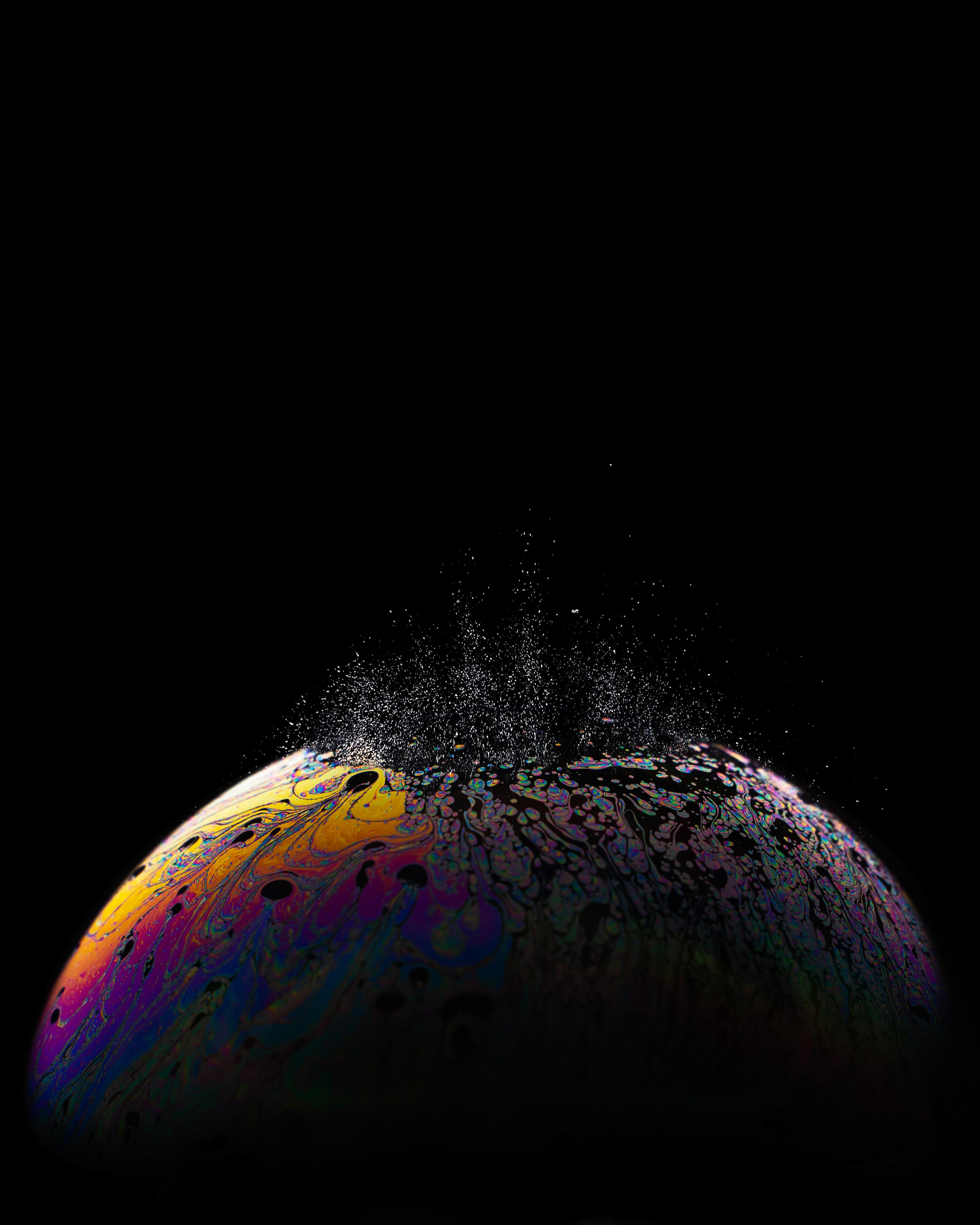 Une bulle de savon colorée éclate sur un fond noir.